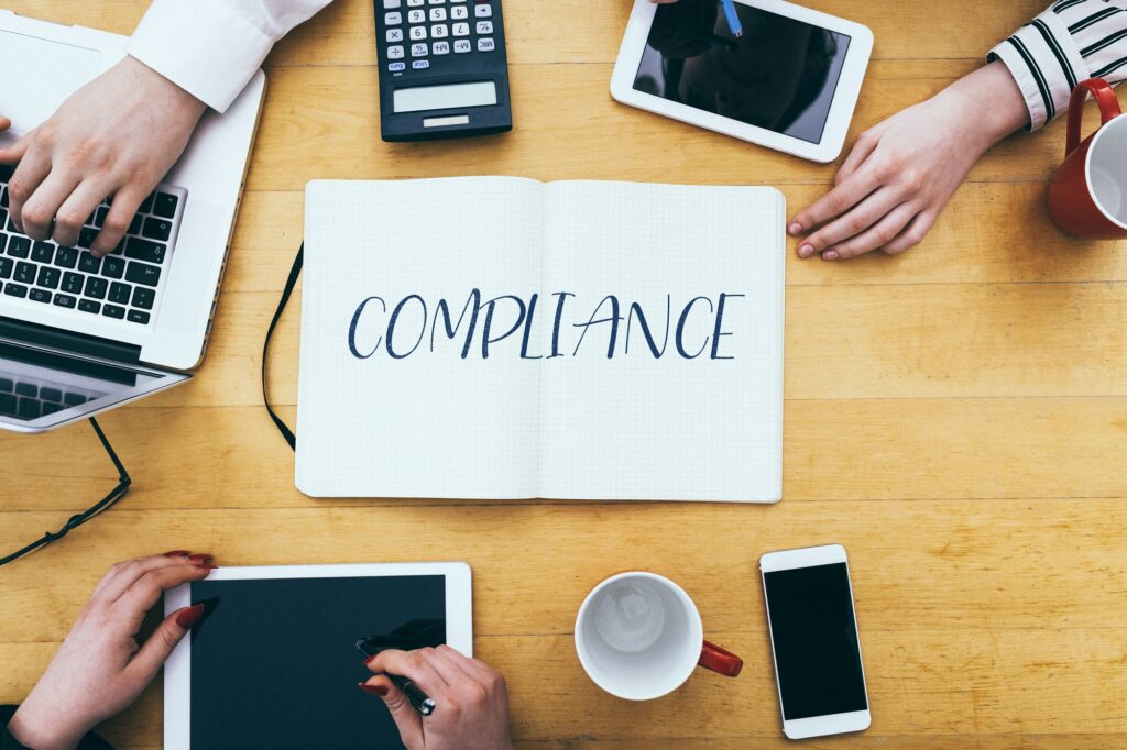 Compliance headline on paper notebook at small business office desk with young adult workers