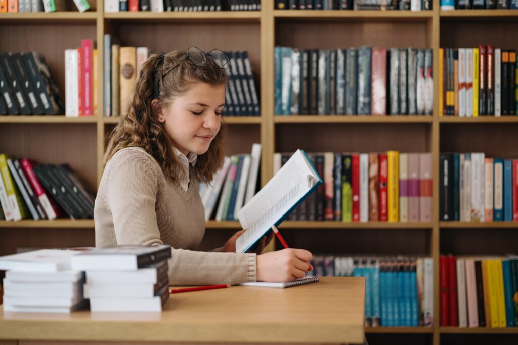 Girl studying among books sitting at the desk among books