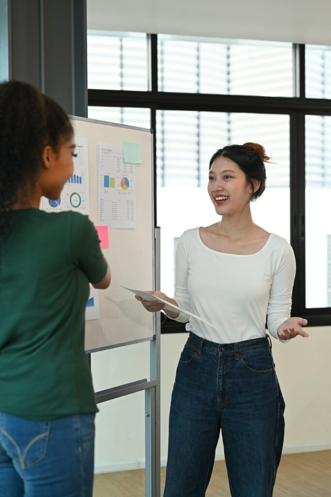 Smiling young creative woman explaining new marketing strategy on whiteboard to her colleagues.