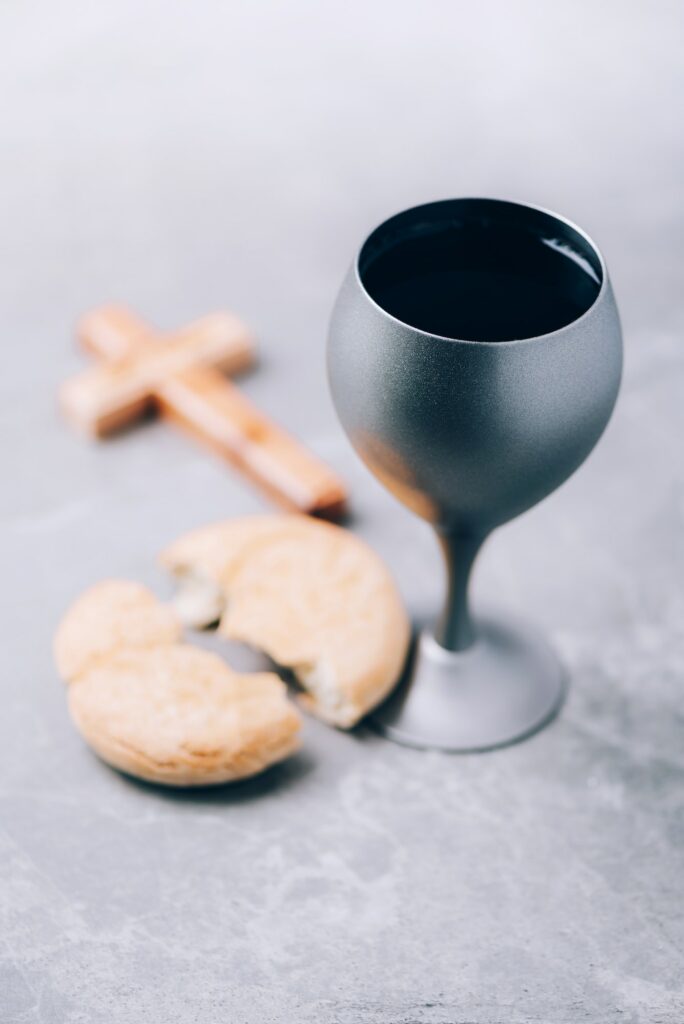 Unleavened bread, chalice of wine, wooden cross on grey background. Christian communion for reminder