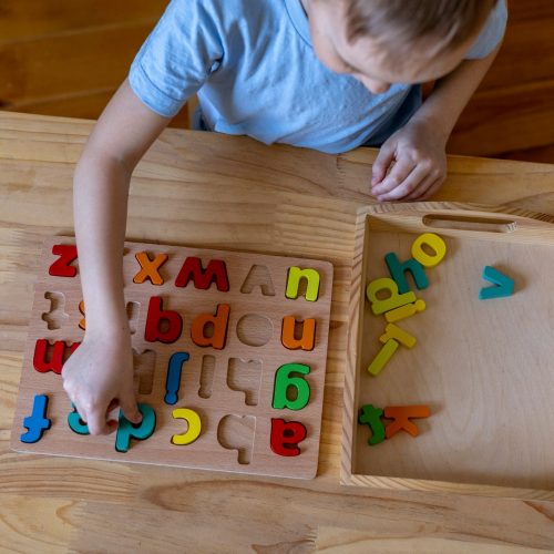Montessori material. Cute little boy playing with wooden letters alphabet. Study of literacy.
