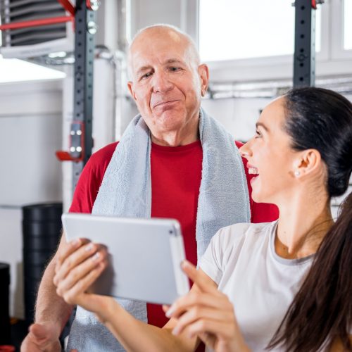 Personal trainer showing results of training on tablet to senior man at the gym