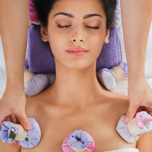 Woman has herbal ball massage in ayurveda spa wellness center